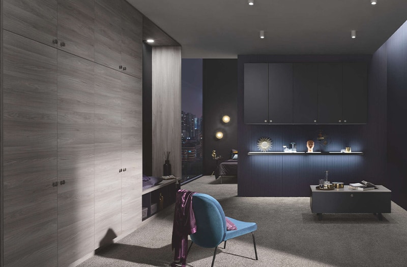 Modern kitchen with blue cabinets, wood paneling, a chair, and minimal decor under soft lighting.