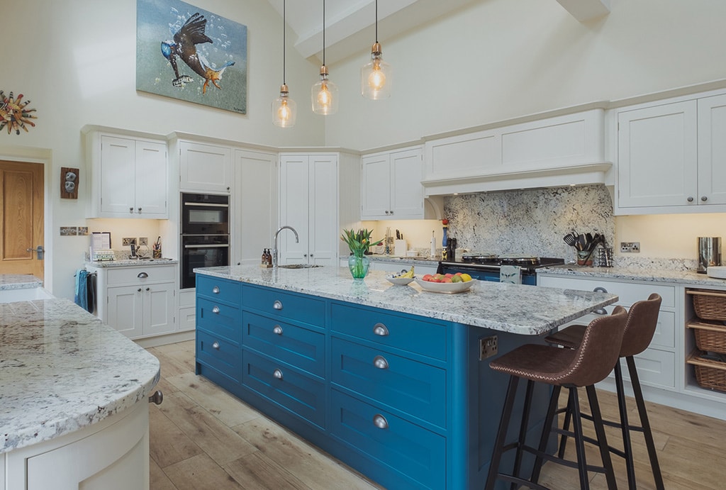 Modern kitchen with a large blue island, marble countertops, and white cabinets.