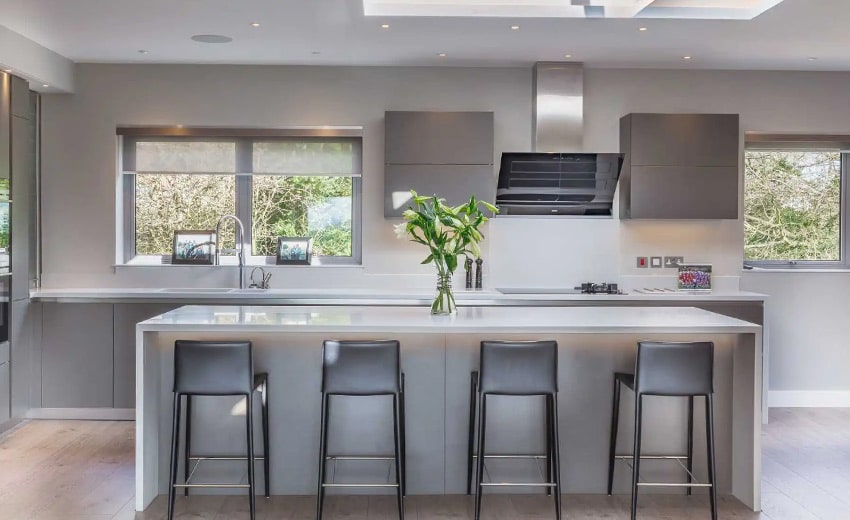 Modern kitchen with a white island, four bar stools, and a vase of flowers on the counter.