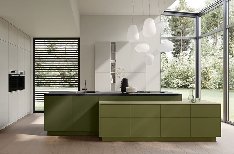 Modern kitchen with green cabinets, pendant lights, and large windows looking out onto greenery.