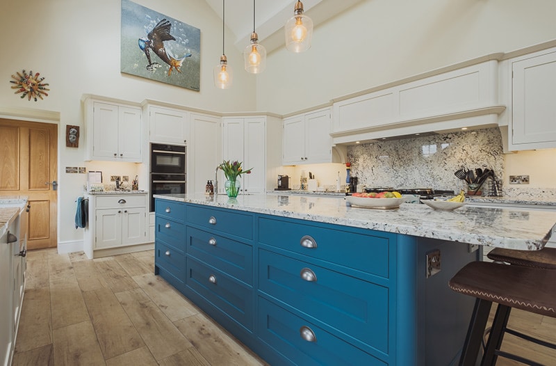 Modern kitchen with a blue island, white cabinets, and pendant lights.
