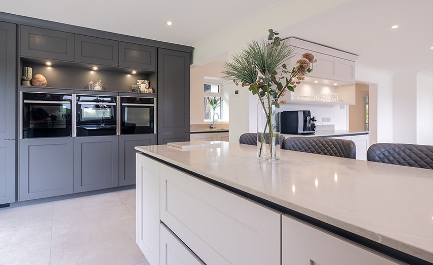Modern kitchen with white countertops, gray cabinets, built-in ovens, and a vase with flowers on the island.