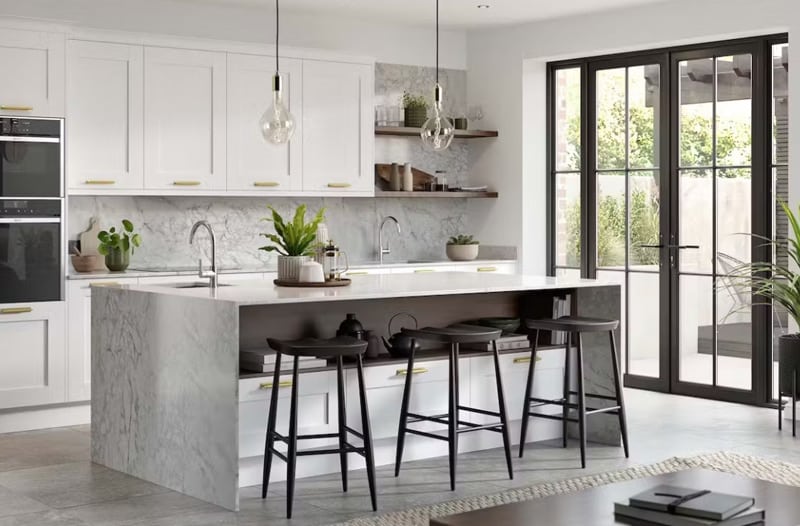 Modern kitchen with white cabinets, marble island, bar stools, and large glass doors letting in sunlight.