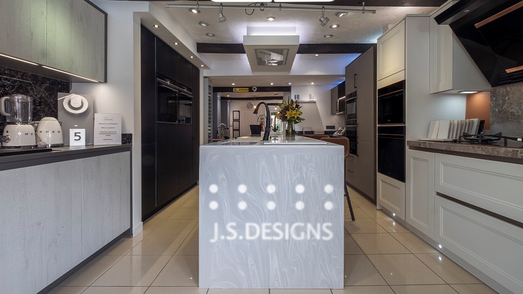 Modern kitchen showroom with white cabinets, appliances, and a center island labeled "J.S. DESIGNS."