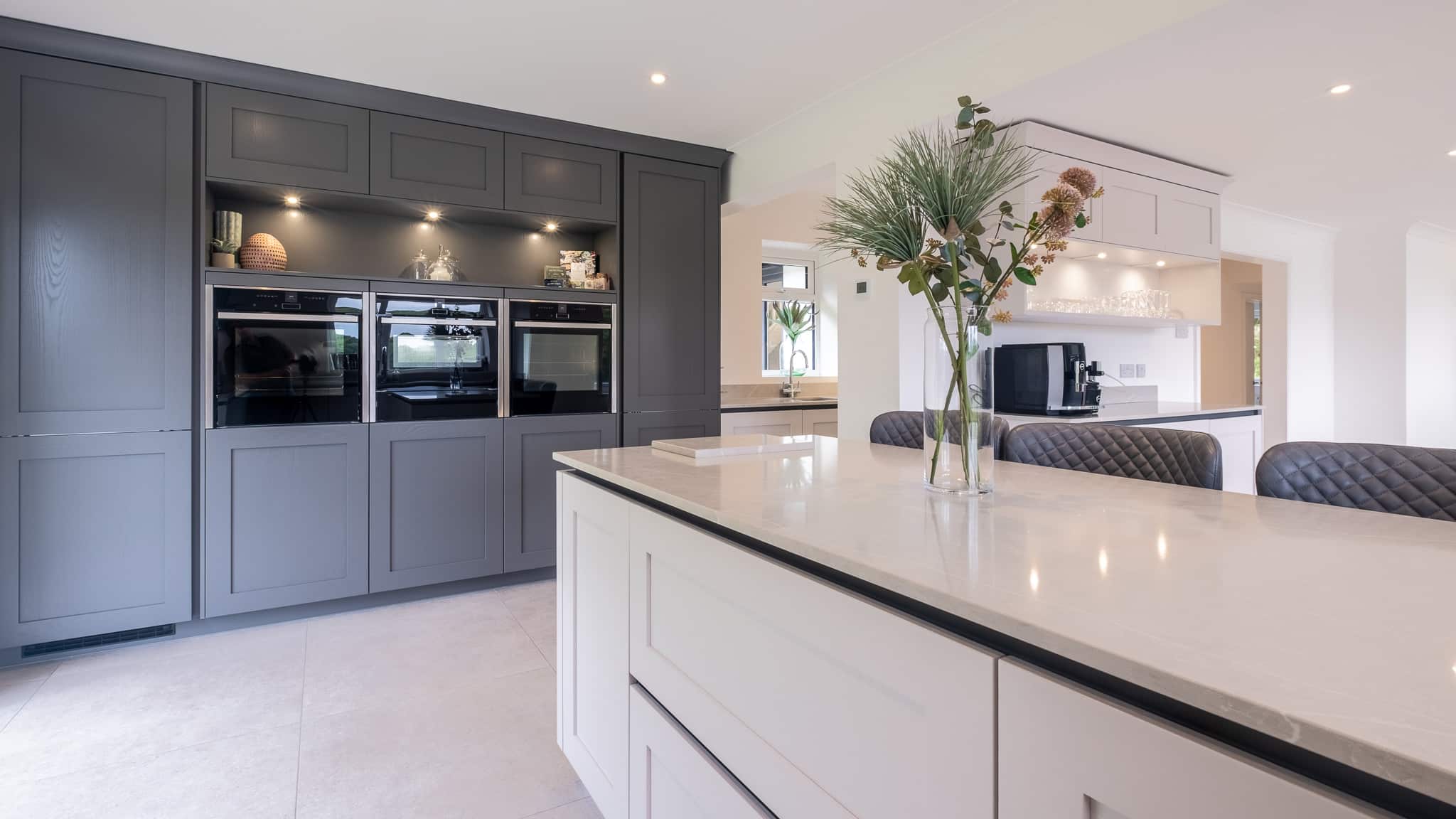 Modern kitchen with a large island, built-in ovens, and a vase of flowers on the countertop.