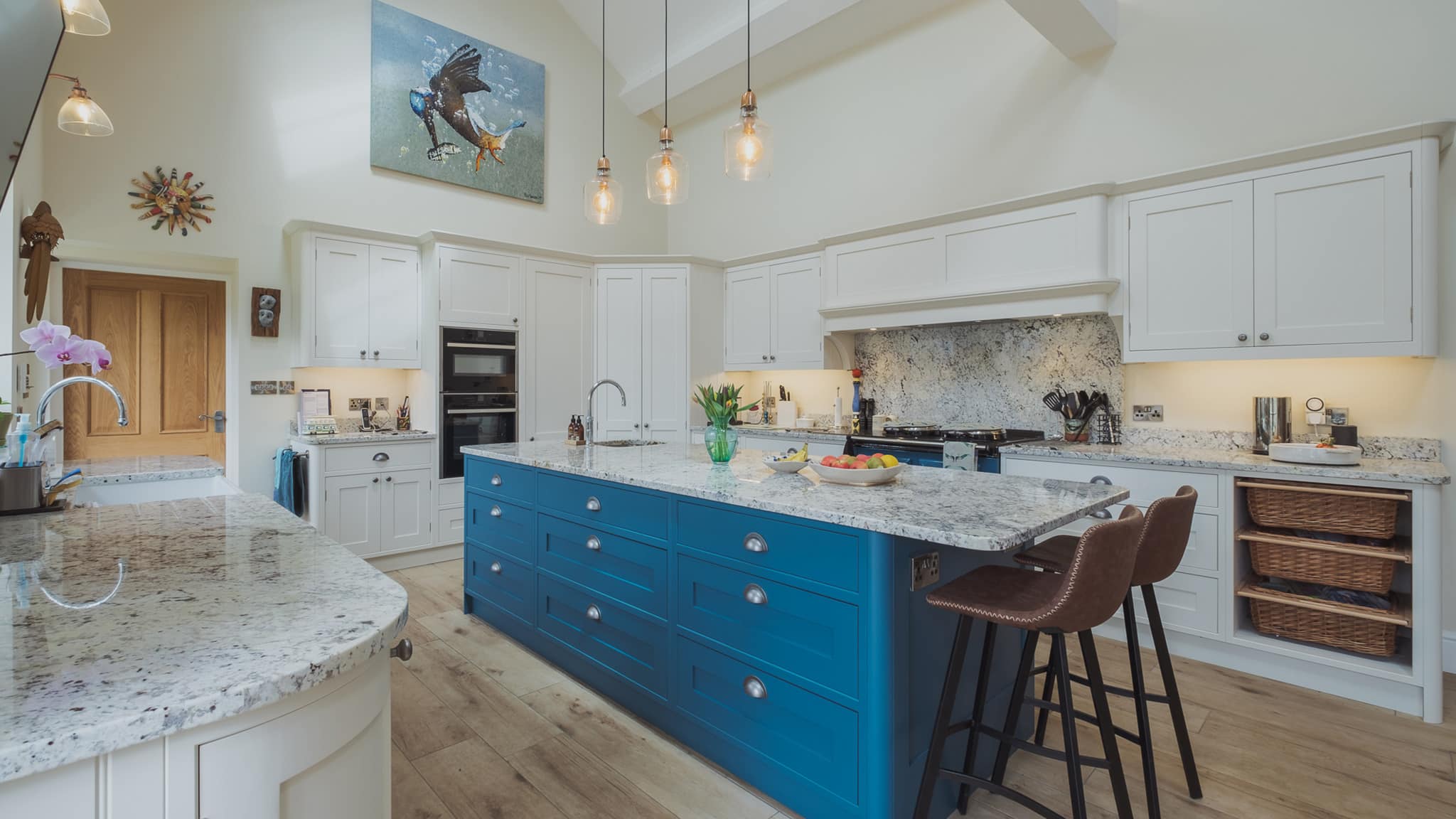 Modern kitchen with white cabinets, a blue island, pendant lights, and two barstools.