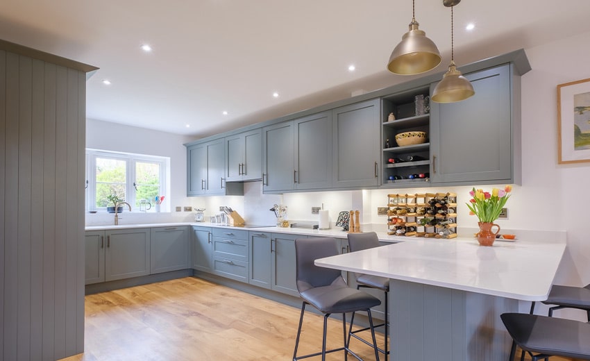 Modern kitchen with grey cabinets, wooden floor, marble countertop, and two chairs at the breakfast bar.