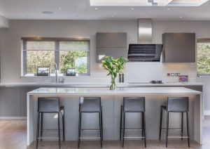 Modern kitchen with gray cabinets, large windows, and four bar stools at a central island.
