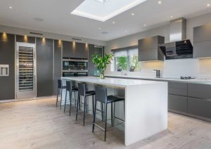 Modern kitchen with gray cabinets, large island, bar stools, and built-in appliances.