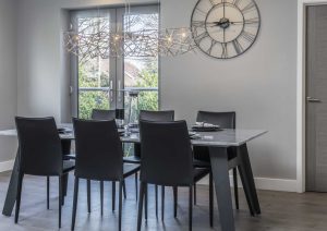 Modern dining room with a black table, six chairs, large wall clock, and glass doors.