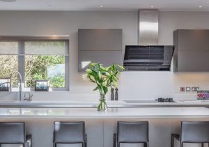 Modern kitchen with a white island, four chairs, and a vase of green flowers on the counter.