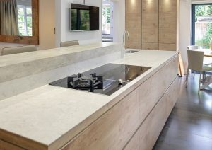 Modern kitchen with a light wood island, gas cooktop, and dining area near large windows.