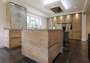 Modern kitchen with wooden cabinets, large island, tiled floor, and bright natural lighting.