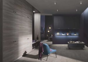 Modern kitchen with gray cabinets, a blue chair, and soft lighting in a sleek, contemporary room.