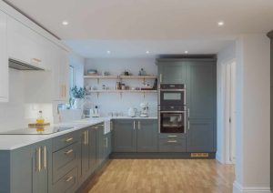 Modern kitchen with grey cabinets, white countertops, wooden floor, and built-in oven.
