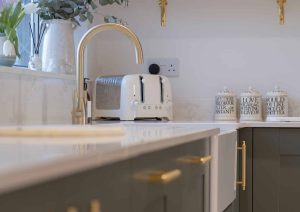 Modern kitchen counter with a white toaster, gold faucet, and jars on a marble surface.