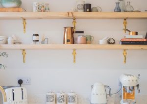 Open wooden shelves with mugs, jars, and kitchen appliances on a white countertop.