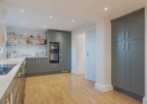 Modern kitchen with grey cabinets, wooden floor, white countertops, and open shelves.