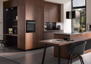 Modern kitchen with wood cabinets, built-in oven, desk area, and large windows letting in natural light.