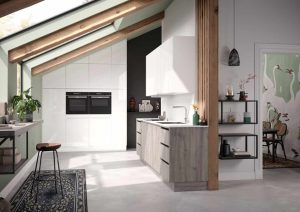 Modern kitchen with large windows, wooden beams, and light cabinets, leading into a small dining area.