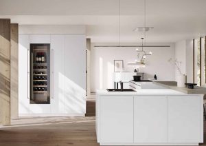 Modern white kitchen with island, built-in wine fridge, and natural light streaming through large windows.