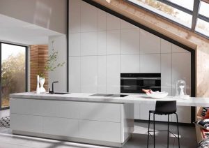 Modern white kitchen with island, built-in oven, and large windows letting in natural light.
