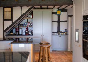 Cozy kitchen with wooden beams, white cabinets, open shelves, and two stools at an island.