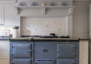 Blue vintage stove in a white kitchen with decorative plates on a shelf above.