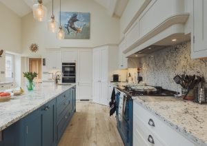 Modern kitchen with white cabinets, blue island, marble countertops, and hanging lights.