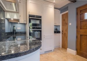 Modern kitchen with white cabinets, dark countertops, a wooden door, and light tile floor.