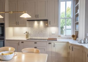 Bright modern kitchen with light cabinets, marble countertops, and a dining table with chairs.