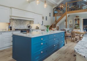 Modern kitchen with a blue island, white cabinets, and wooden floors, featuring a staircase and loft.