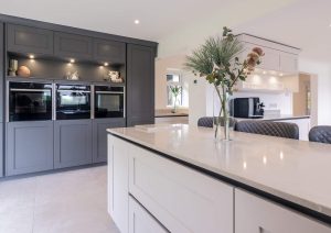 Modern kitchen with a large island, dark cabinets, built-in ovens, and a vase with flowers on the counter.