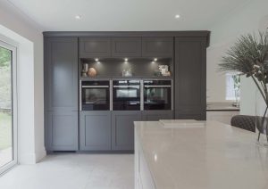 Modern kitchen with dark cabinets, built-in ovens, and a large white island countertop.