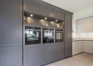 Modern kitchen with built-in grey cabinets and three stainless steel ovens.