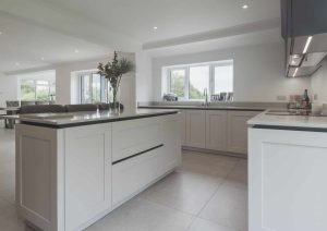 Modern white kitchen with island, large windows, and open dining area in the background.