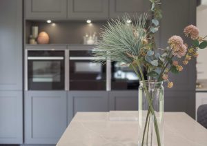A modern kitchen with grey cabinets and a glass vase of flowers on the counter.