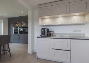Modern kitchen with light cabinets, built-in appliances, a coffee machine, and barstools.