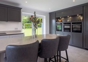 Modern kitchen with grey cabinets, a large island, three chairs, and a vase with flowers on the counter.