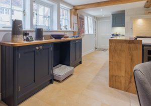 Modern kitchen with blue cabinets, wood countertop, tiled floor, and large windows letting in natural light.