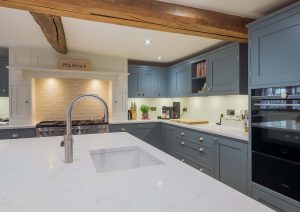 Modern kitchen with blue cabinets, white countertops, a sink island, and wooden beam across the ceiling.