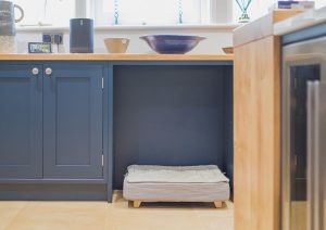 A dog bed in a built-in nook under a kitchen counter next to blue cabinets.