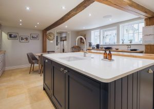 Modern kitchen with a large island, wooden beams, and natural light from multiple windows.