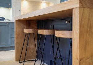 Wooden kitchen island with three bar stools and blue cabinetry in the background.