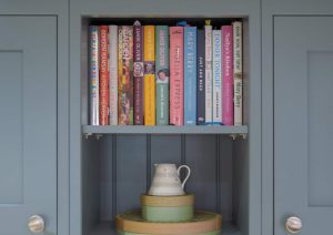 Books and a pitcher on shelves in a gray cabinet.
