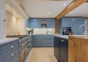 Modern kitchen with blue cabinets, wood accents, and built-in appliances under bright lighting.
