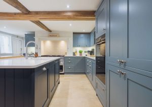 Modern kitchen with blue cabinets, a large island, wooden beams, and bright lighting.