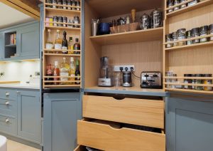Open kitchen pantry with shelves for spices, jars, and appliances, plus two large open drawers below.