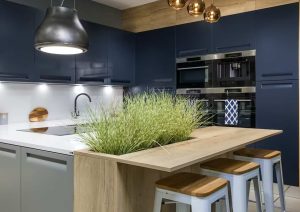 Modern kitchen with blue cabinets, built-in ovens, and a wooden island with plants and bar stools.
