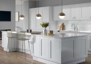 Modern white kitchen with island, barstools, pendant lights, and a vase of flowers on the counter.